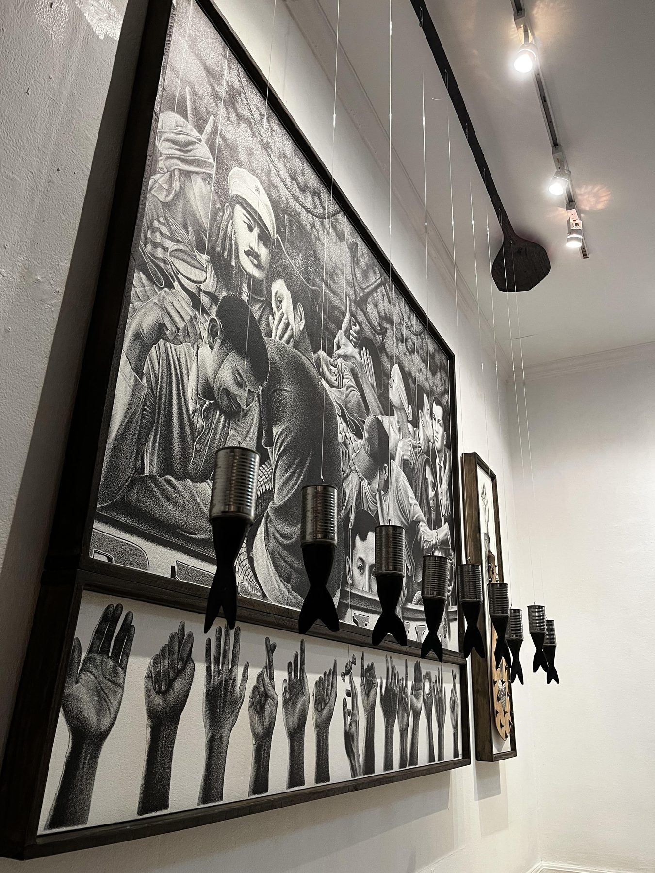 Close view of Langit Lupa: tin cans with black tail fins hanging on nylon lines before the drawings